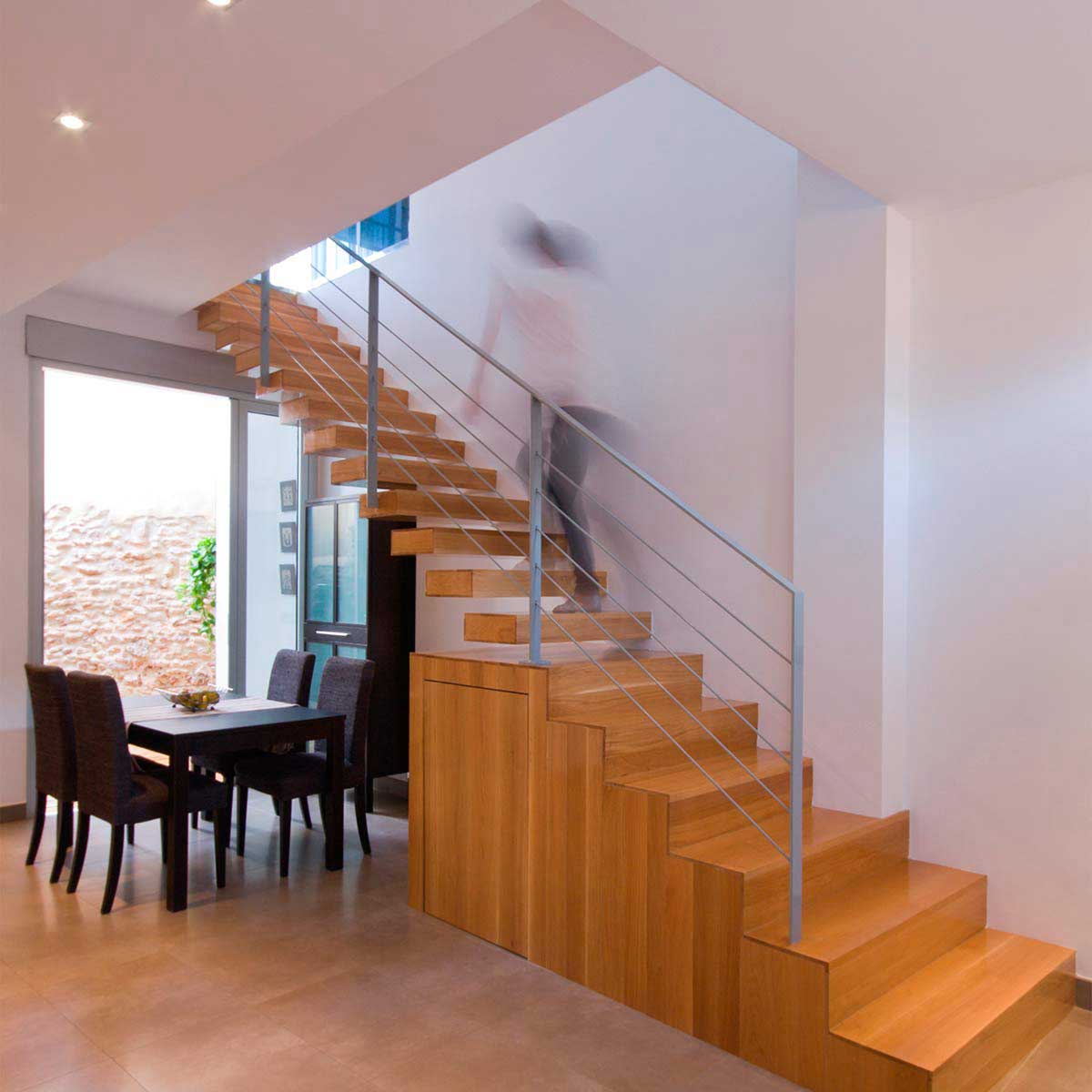 Interior de vivienda accesible con escalera volada de madera con gran ventanal que da paso a la luz natural